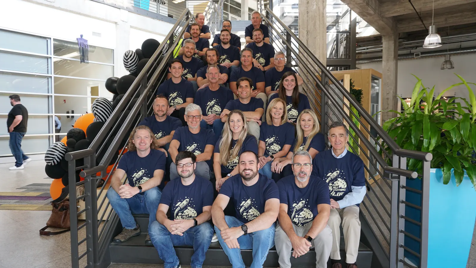 The Help Lightning team seated on office stairs in matching Help Lightning 4.0 shirts.