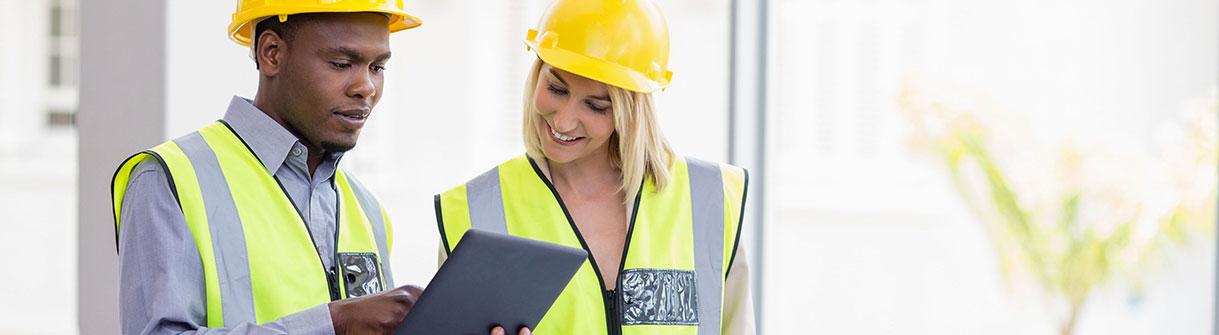 Two workers wearing hard hats and looking at a tablet, overcoming a technology adoption curve